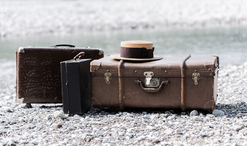 Antike Koffer mit Herrenhut am Ufer